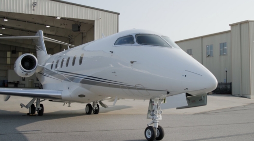 White private jet with navy and gray stripes parked on the ramp outside an open hangar